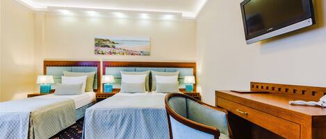 Quarto de hotel com duas camas, uma escrivaninha, uma cadeira, uma televisão e um quadro na parede.