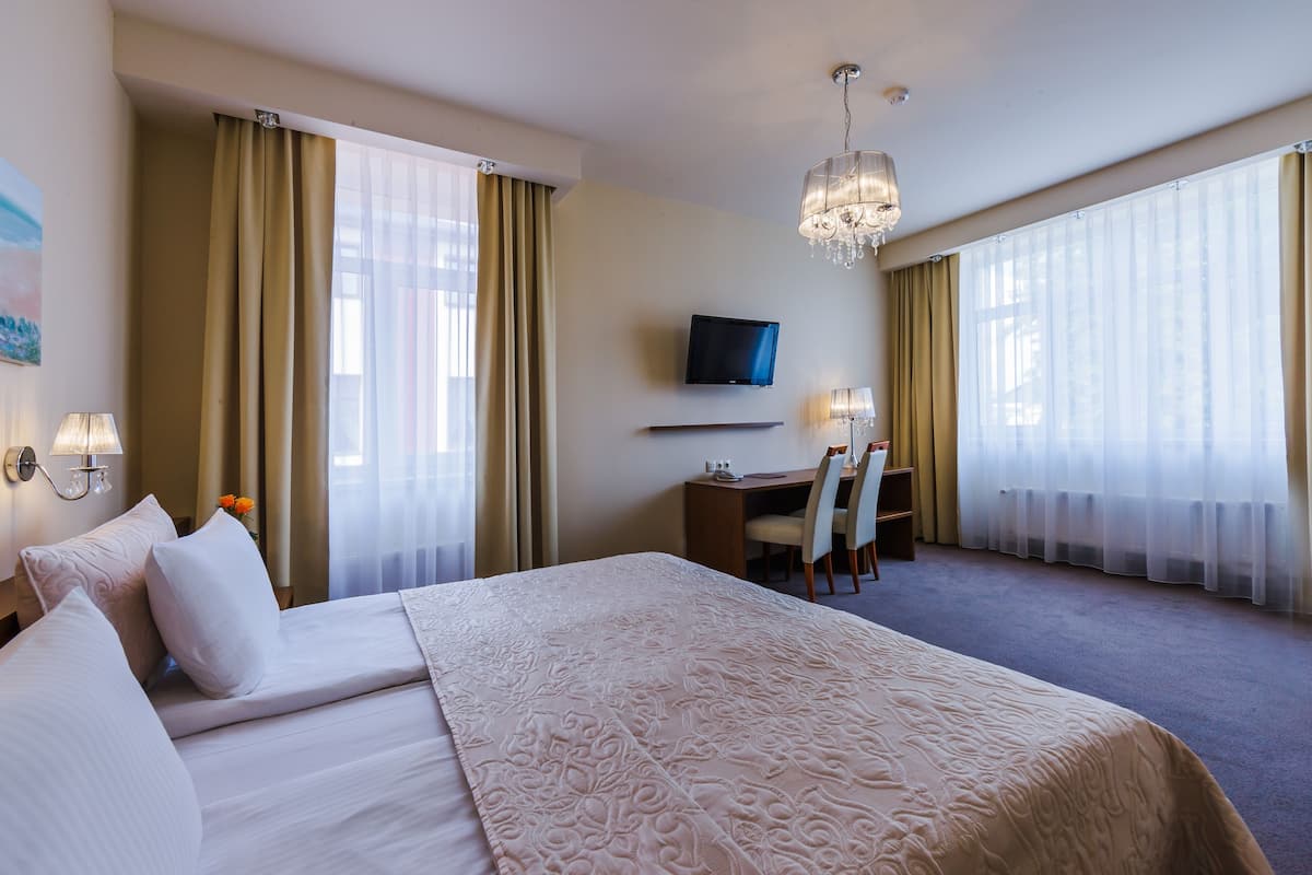 Quarto de hotel com uma cama grande, uma escrivaninha com cadeira, televisão e um candelabro.