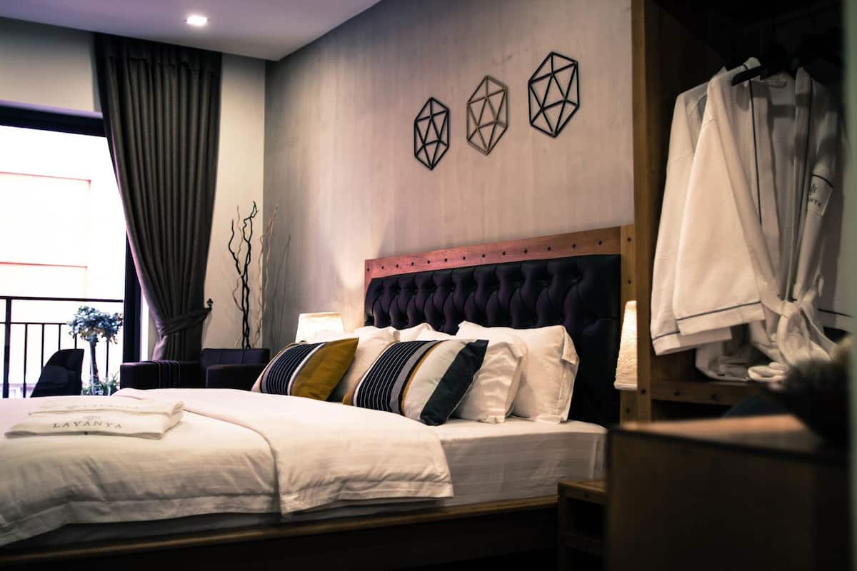 Habitación de hotel con cama, cabecera, mesita de noche, lámpara, armario y ventana con cortinas.