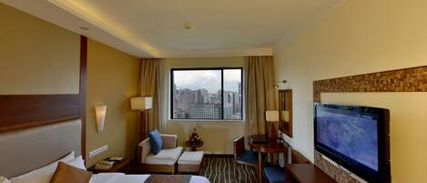 A hotel room with a large bed, a desk, a chair, a TV, and a view of the city through the window.