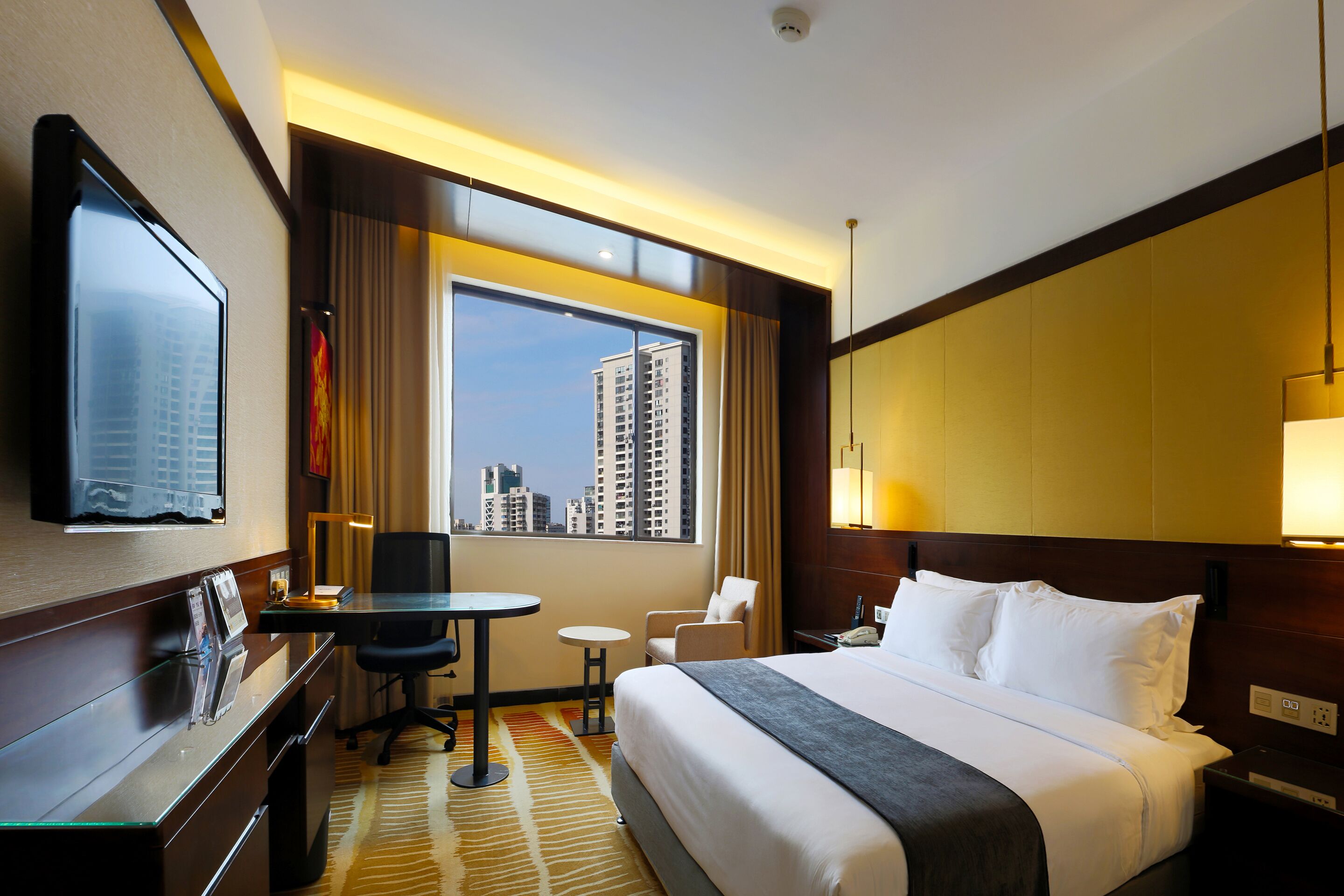 Hotelkamer met een groot bed, een bureau met stoel, een televisie, een raam met uitzicht op de stad en een kleine tafel.