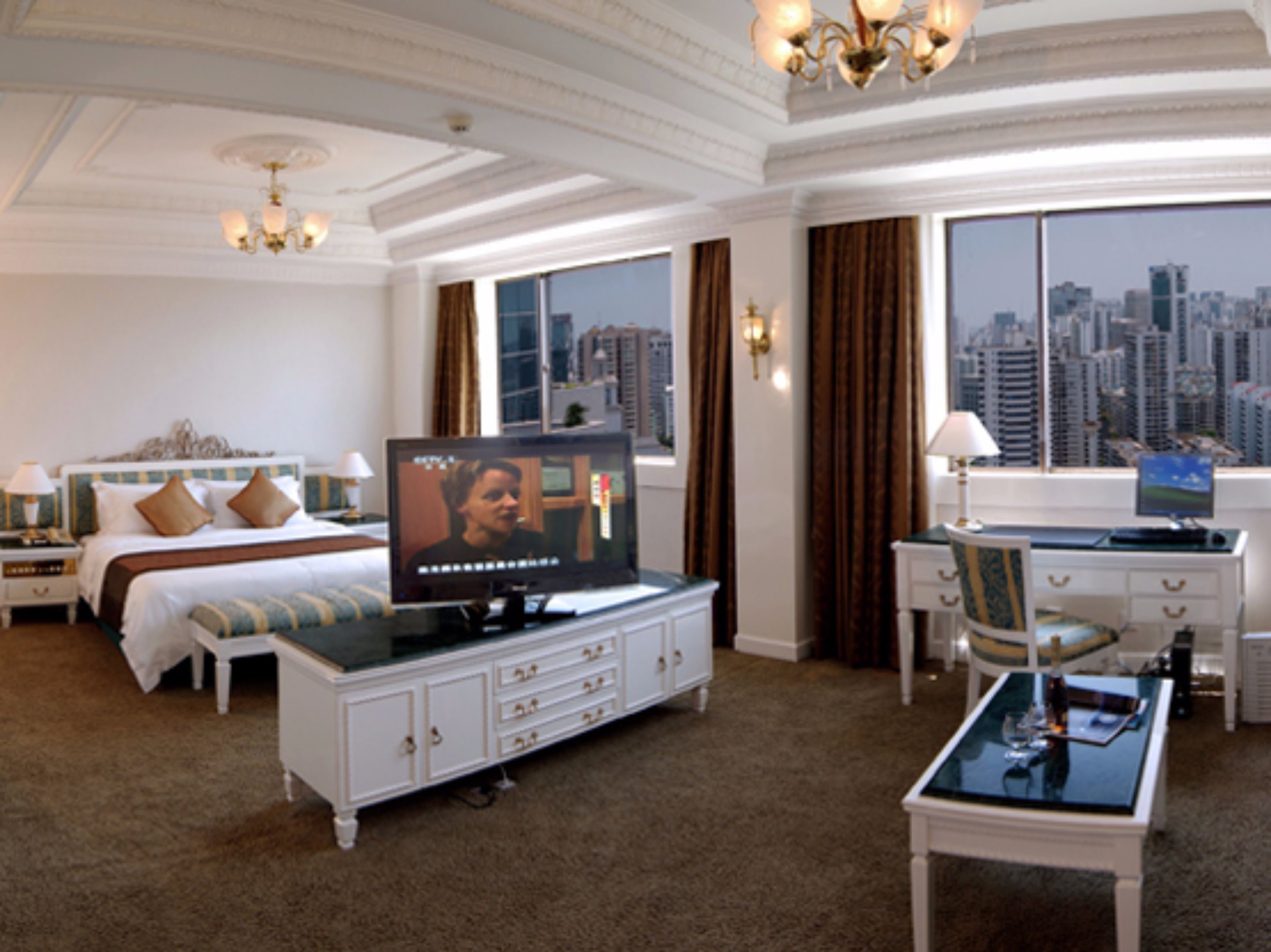 A hotel room with a bed, a television, a desk, and a view of the cityscape.