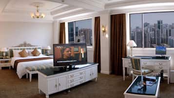 A hotel room with a bed, a television, a desk, and a view of the cityscape.
