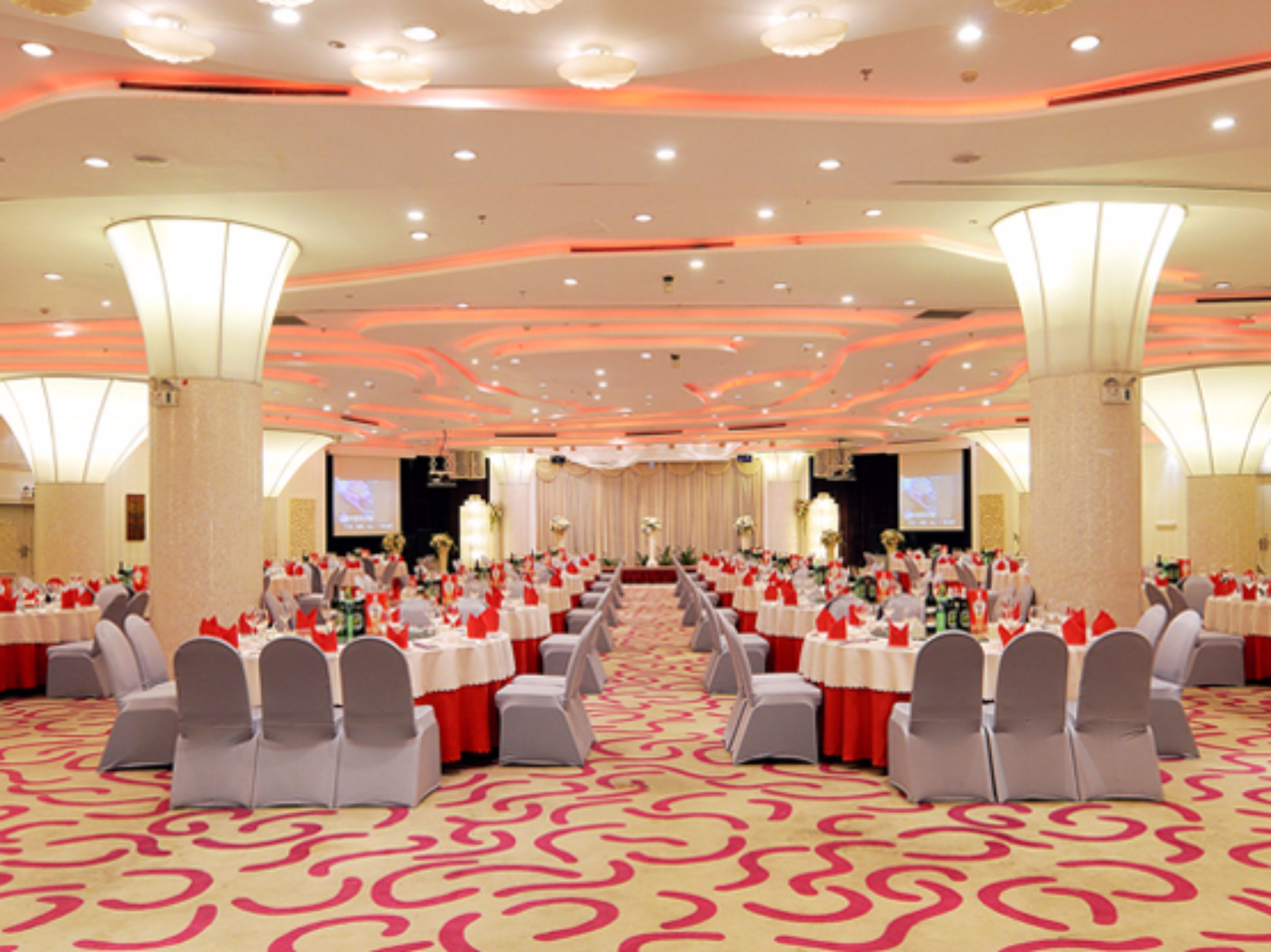 A banquet hall with rows of tables and chairs, a patterned carpet, and a modern ceiling design.