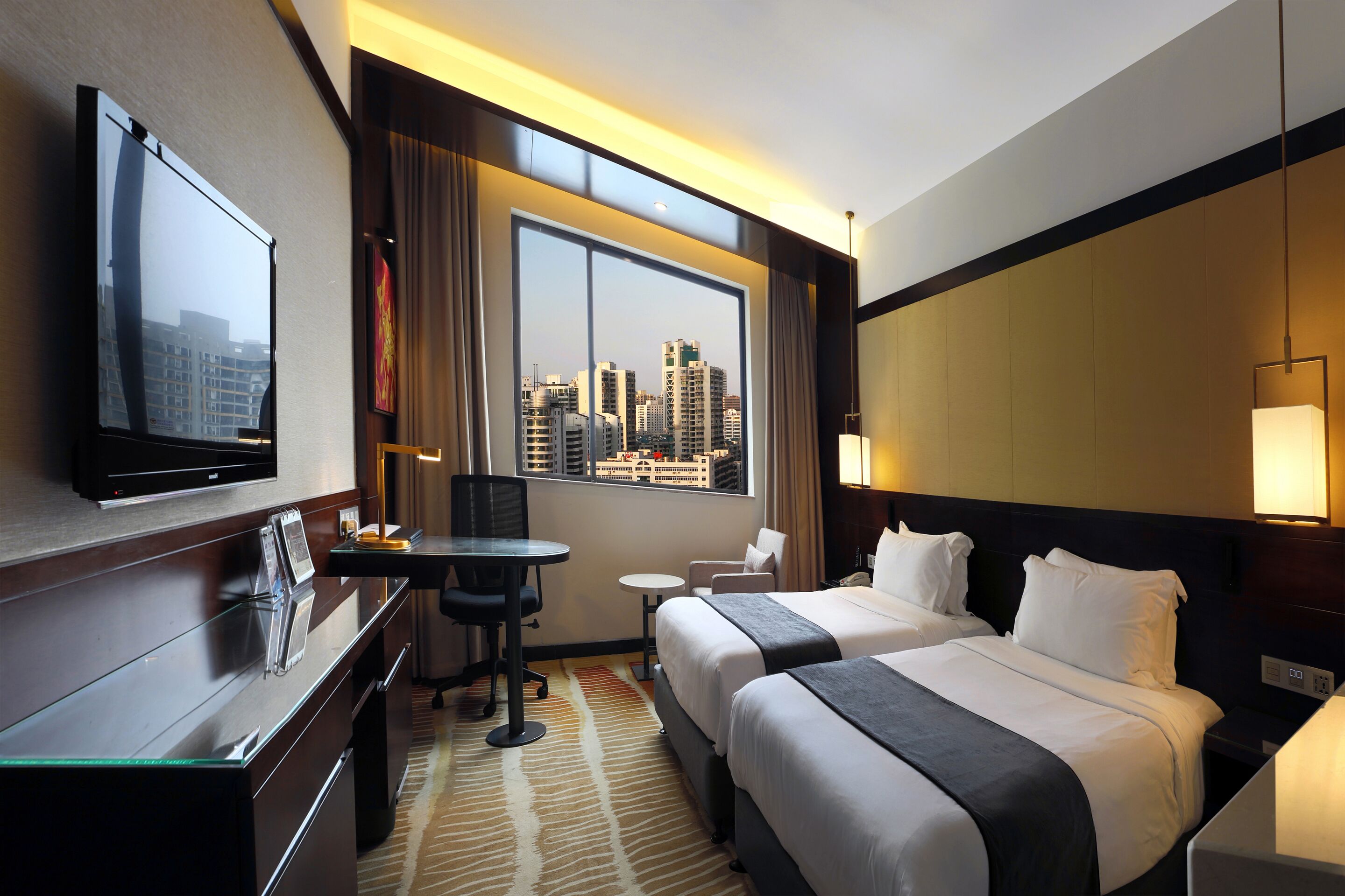 Habitación de hotel con dos camas, un escritorio, una silla, un televisor y una ventana con vista a la ciudad.