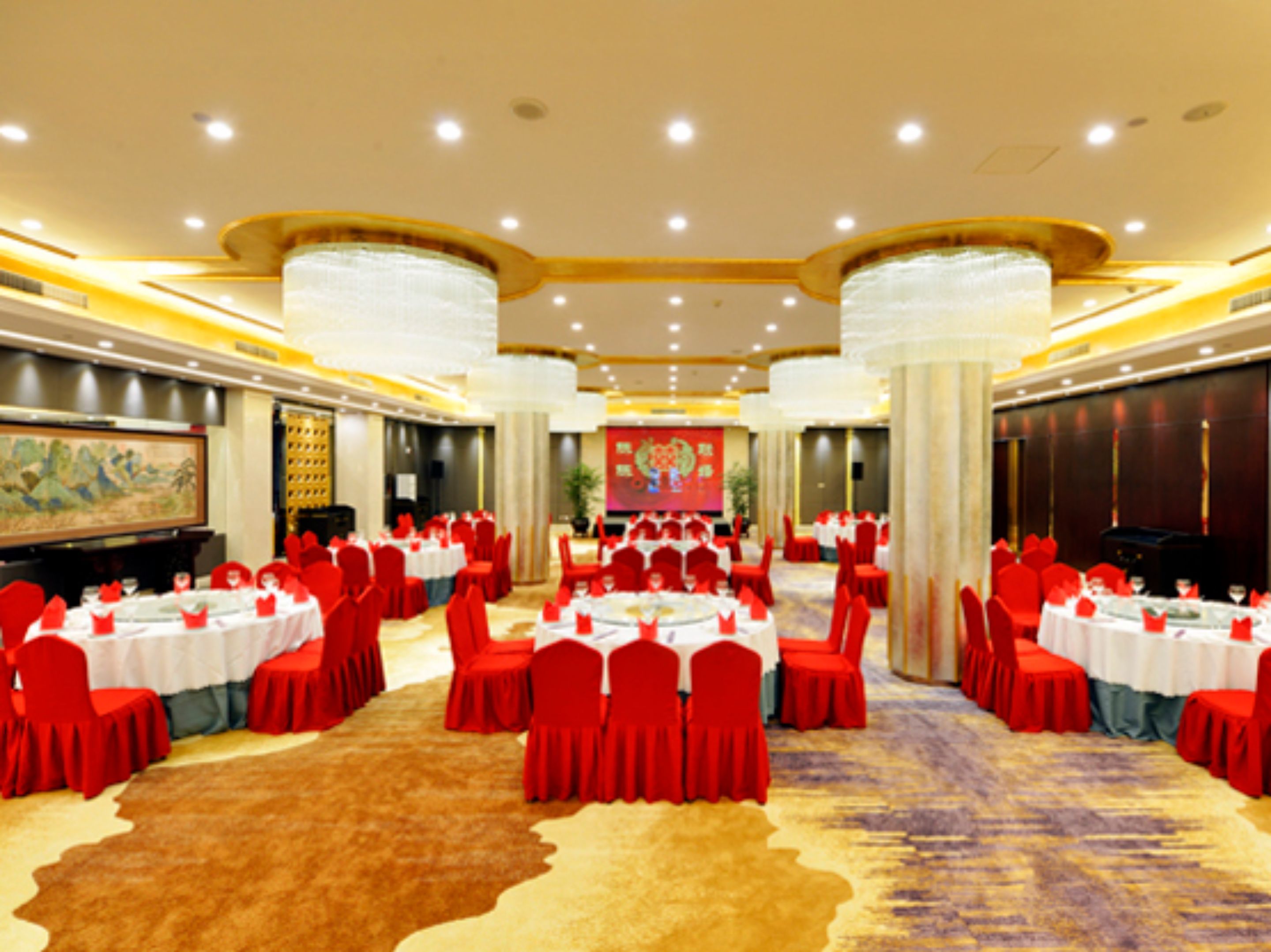 A large banquet hall with round tables, red chairs, and a central stage.
