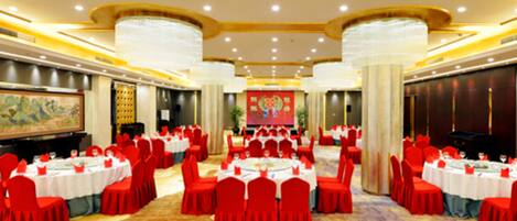 A large banquet hall with round tables, red chairs, and a central stage.