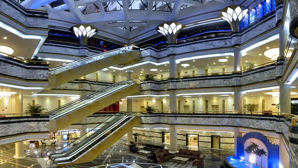 Un atrio de varios niveles con suelos de mármol, escaleras mecánicas y una fuente central.