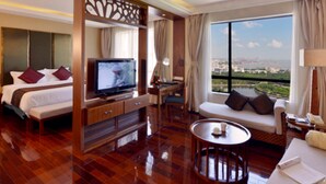 Habitación de hotel con cama, televisor, sofá y vistas a la ciudad.