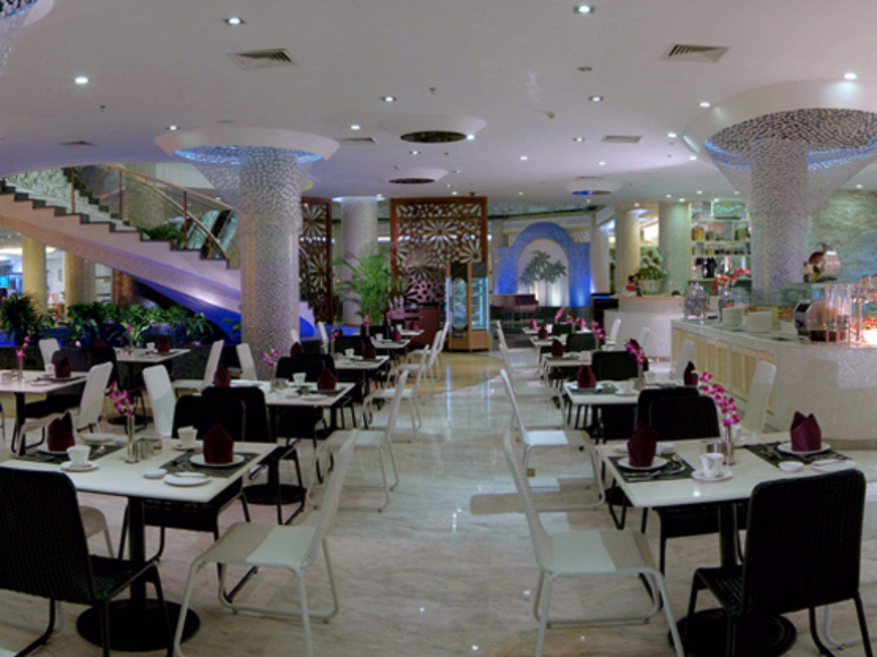 A modern restaurant with white tables and chairs, a staircase, and decorative pillars.