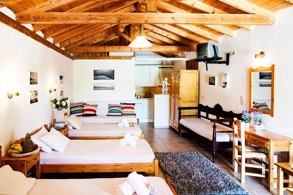 Una habitación acogedora con tres camas de madera, un banco de madera, una mesita y un televisor montado en la pared.