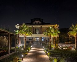 A two-story house with a covered patio, palm trees, and a well-lit entrance.