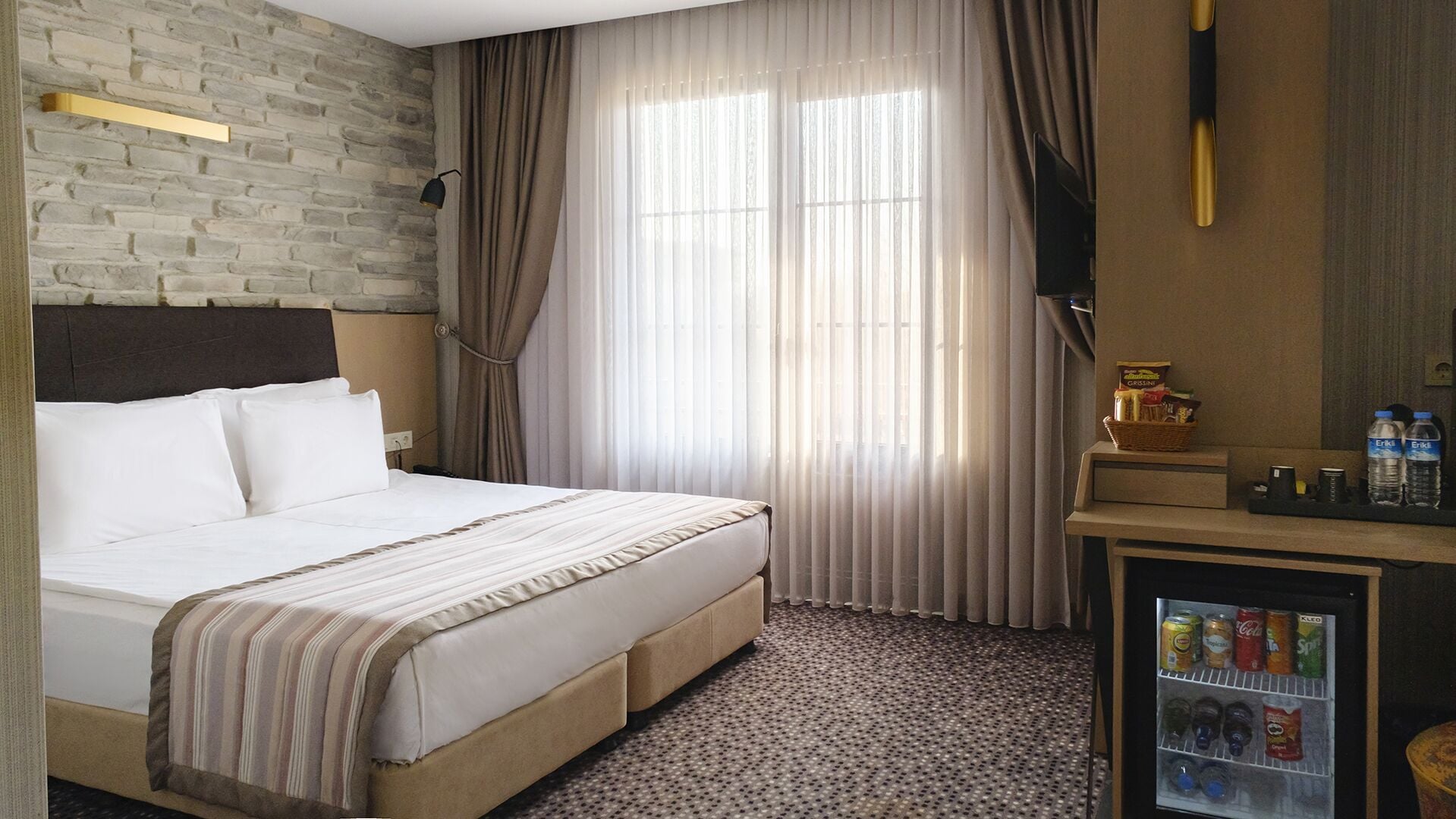 A hotel room with a bed, a minibar, a television, and a brick wall.