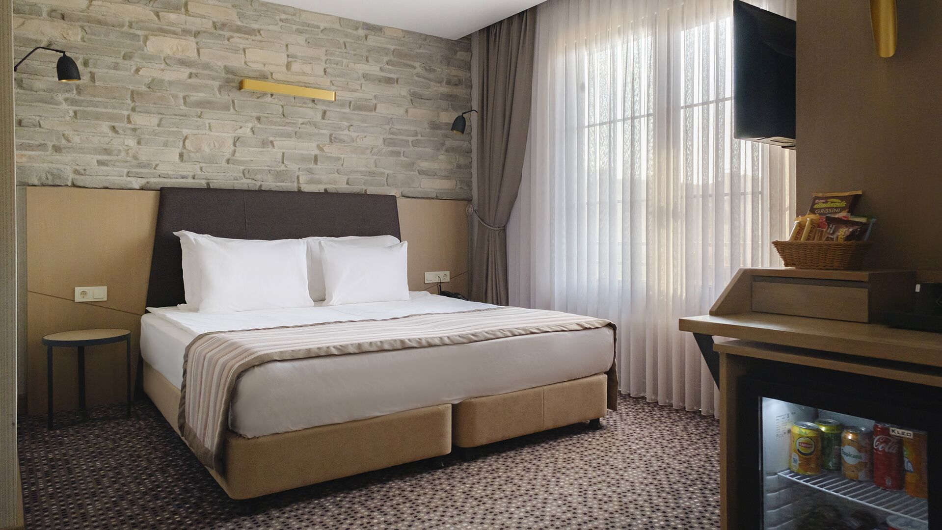 Ein Hotelzimmer mit einem Bett, einem kleinen runden Tisch, einem Fernseher und einer Minibar.