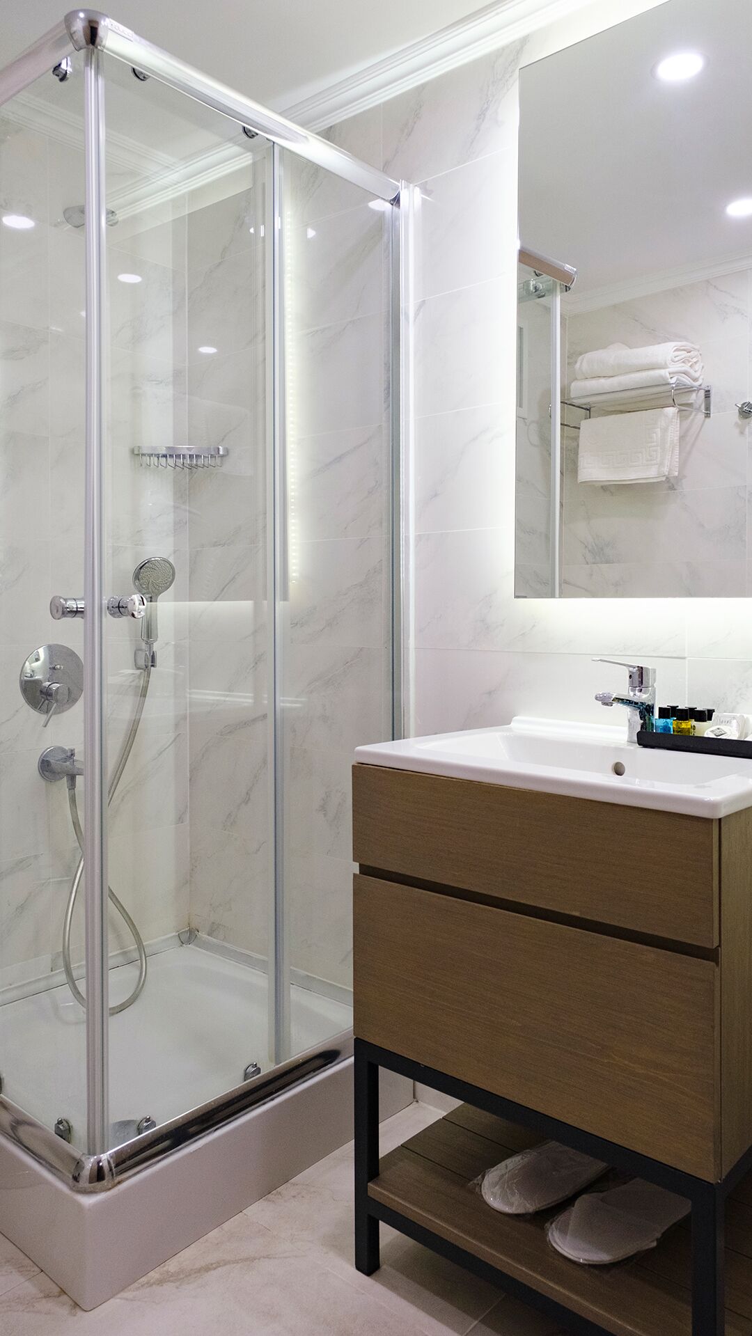 Een moderne badkamer met een douchecabine van glas, een houten wastafelmeubel met spiegel, en een betegelde vloer.