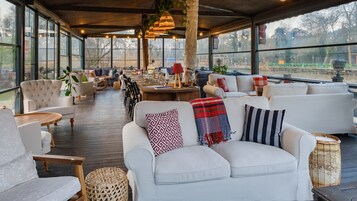 Un espacio interior amplio con piso de madera, sofás blancos y un ventanal con vistas al exterior.
