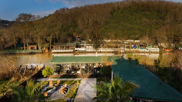 Un restaurante junto al lago con terraza al aire libre y vistas al lago y colinas boscosas.
