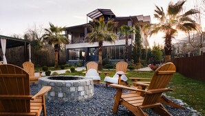 Un patio moderno al aire libre con sillas Adirondack, un hogar de piedra y vistas a una casa contemporánea con balcón.