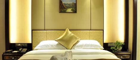 A hotel room with a large bed, two bedside lamps, a painting on the wall, and a plant on the nightstand.