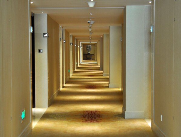 A long, narrow hotel corridor with a carpeted floor and a central light fixture.