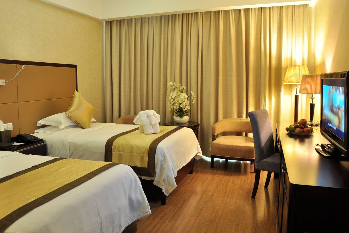A hotel room with two beds, a desk with a television, a chair, a lamp, and a vase with flowers.
