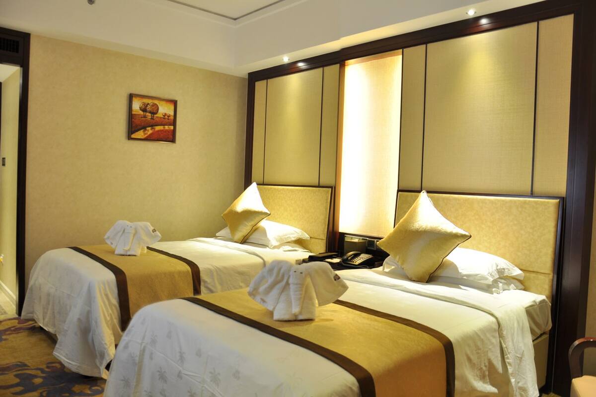 A hotel room with two beds, each with a headboard, bedside tables, lamps, and a painting on the wall.
