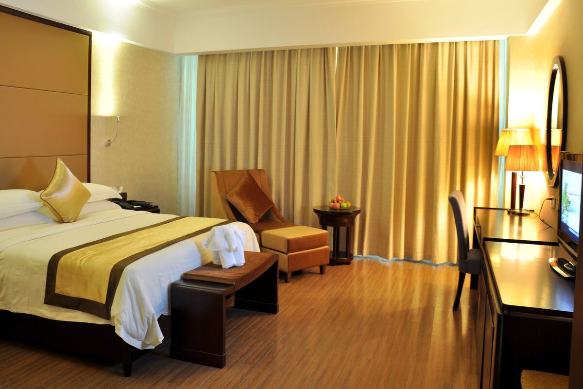 A hotel room with a large bed, a desk, a chair, a small table with fruit, and a TV.