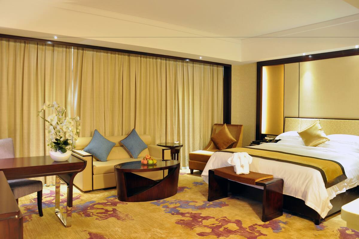 A hotel room with a large bed, a sofa, a coffee table, and a desk.