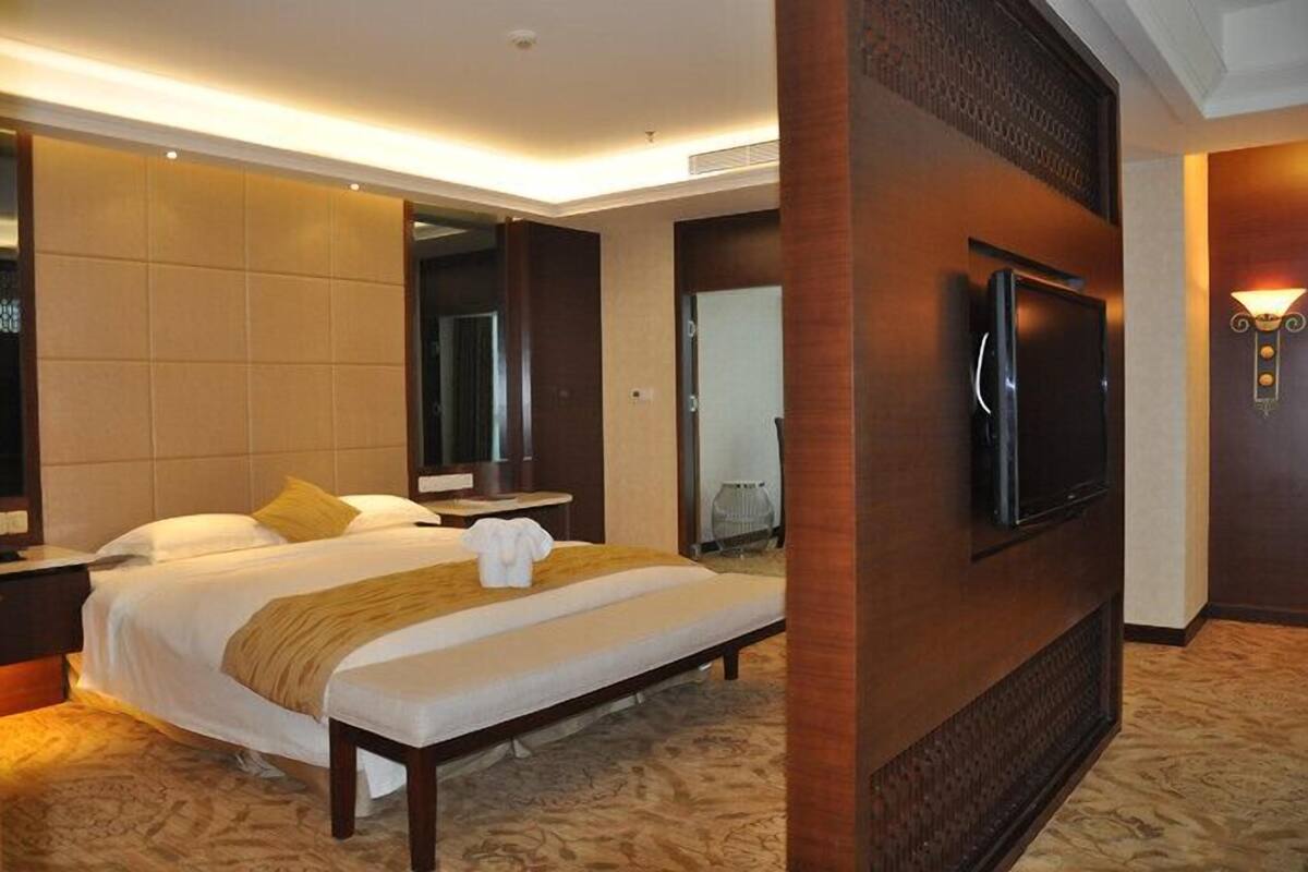 A hotel room with a large bed, a flat-screen TV mounted on the wall, and a wooden accent wall.