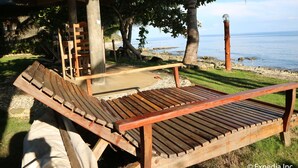 A wooden lounge chair and a small table under a wooden structure by the beach.
