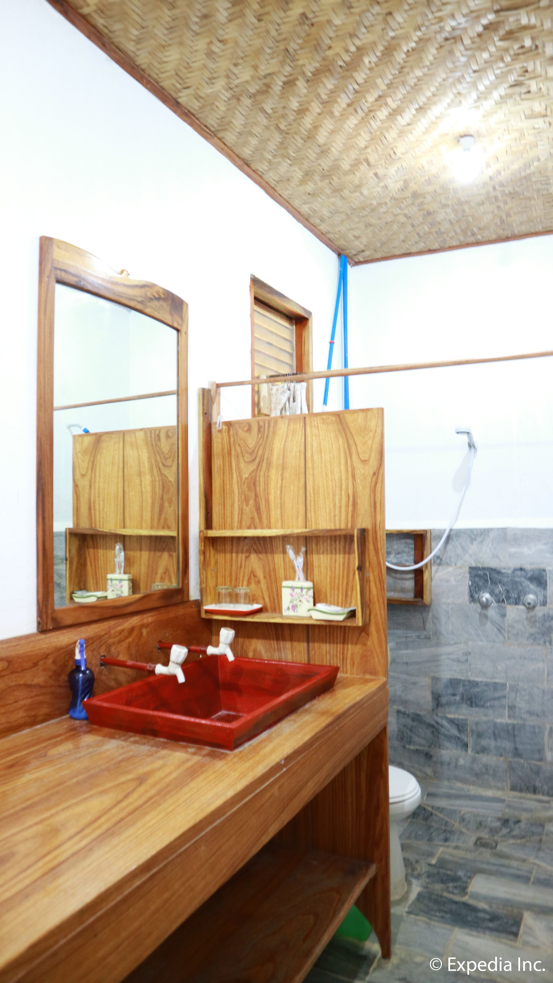 A bathroom with a wooden vanity, a red sink, a mirror, a shower, and a toilet.