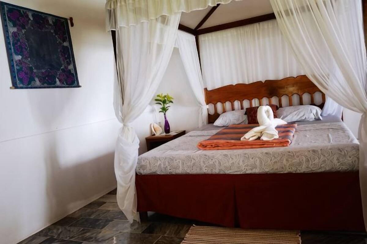 A bed with a wooden headboard, white curtains, and a white towel on the bed.