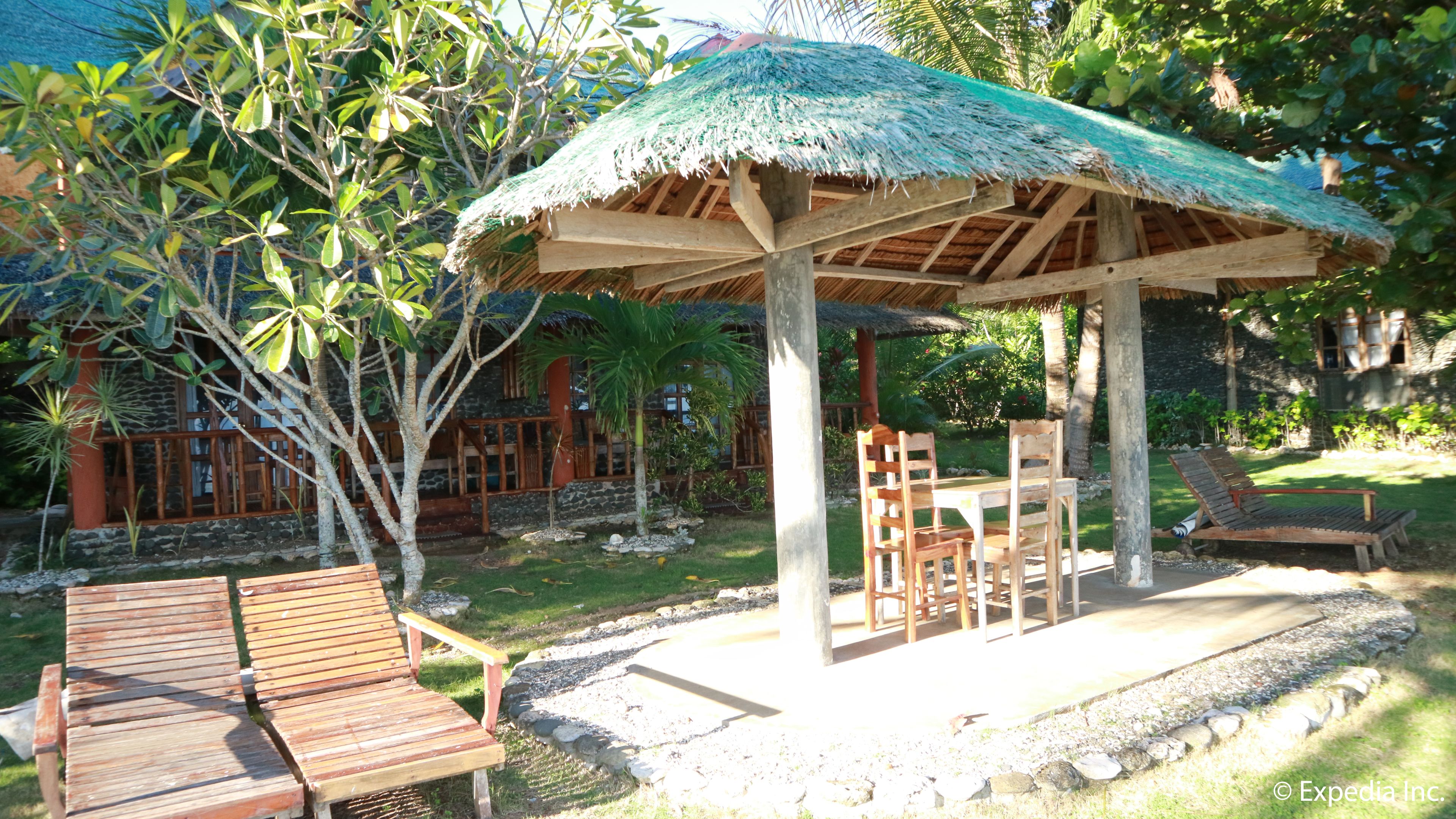 A wooden gazebo with a thatched roof, surrounded by a stone wall and lush greenery.