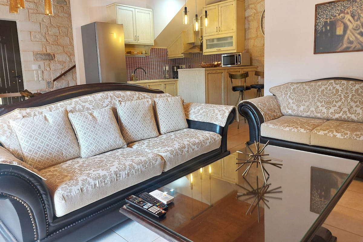 A living room with a sofa, a glass coffee table, and a kitchen in the background.