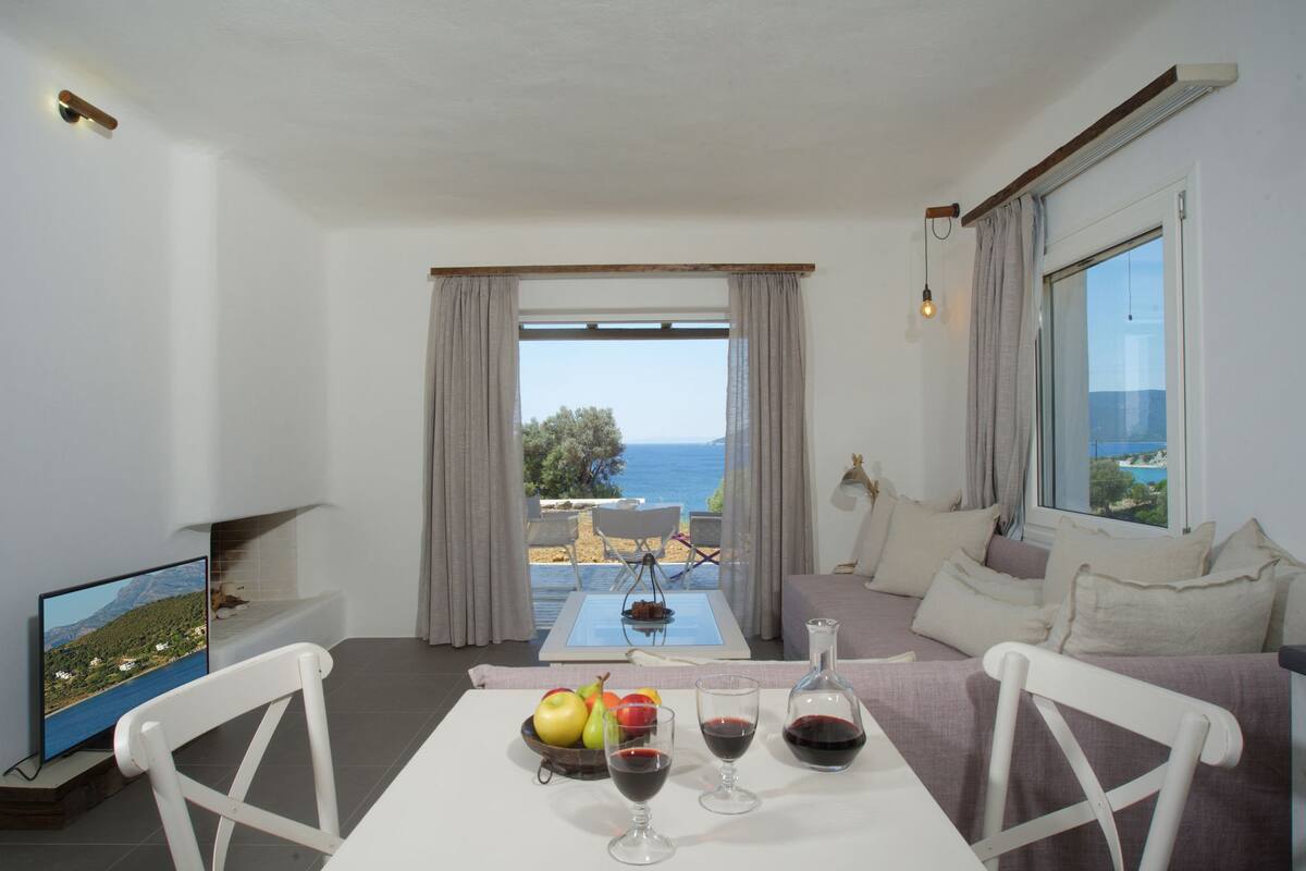 Une pièce comprenant une table à manger dressée pour deux personnes, un canapé, un téléviseur et une vue sur la mer.