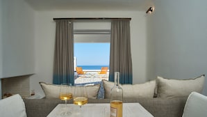 Une pièce avec vue sur la mer, un canapé, une table avec une bouteille et des verres, et une fenêtre avec des rideaux.