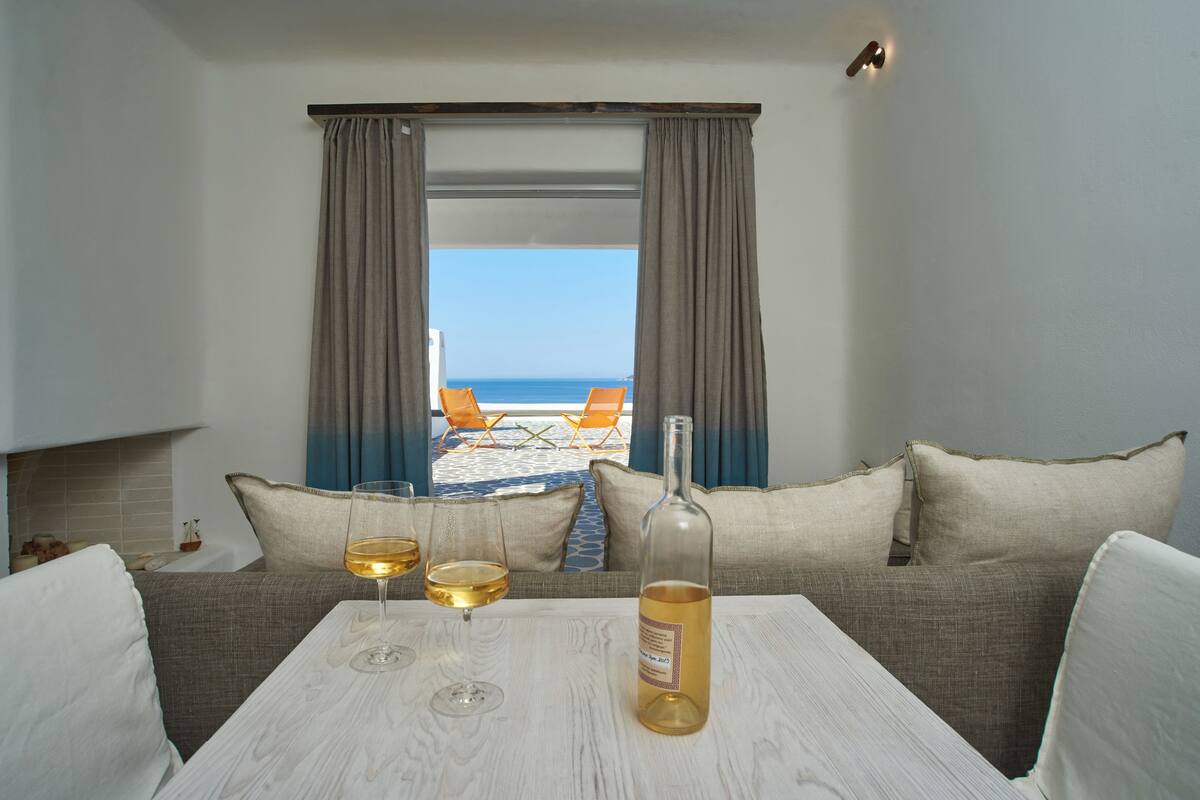Une pièce avec vue sur la mer, un canapé, une table avec une bouteille et des verres, et une fenêtre avec des rideaux.