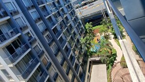 Um edifício residencial alto, com várias varandas e área de piscina com palmeiras.