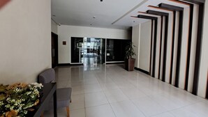 Um hall amplo com design moderno, com balcão de recepção, área de estar e uma grande planta em vaso.