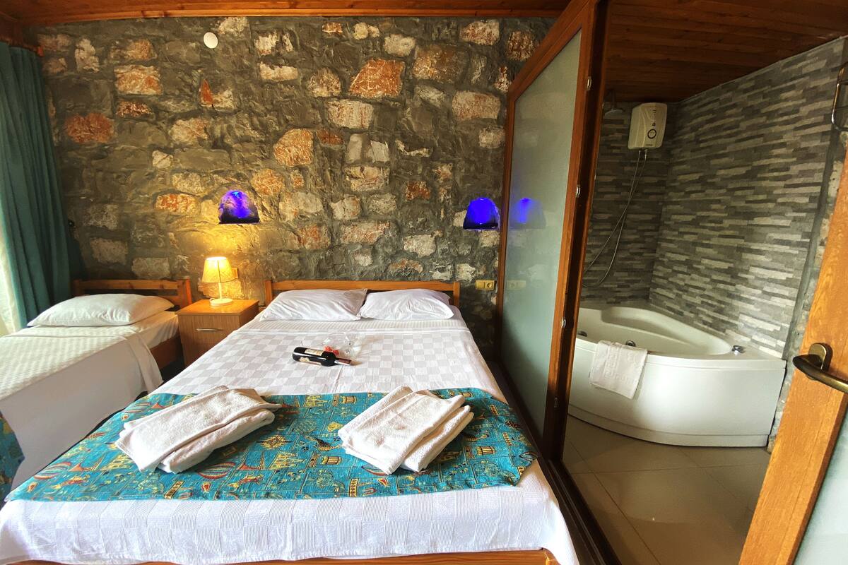 A room with a stone wall, a bed with a checkered bedspread, two towels, a bottle, and a bathtub.