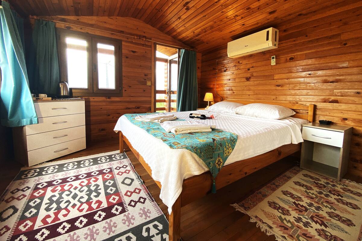 A wooden cabin bedroom with a bed, nightstand, dresser, and a window with curtains.
