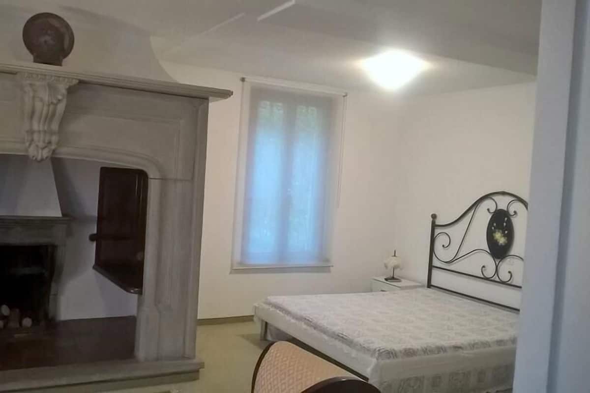 Quarto com lareira, cama, janela com cortinas e mesa de cabeceira.