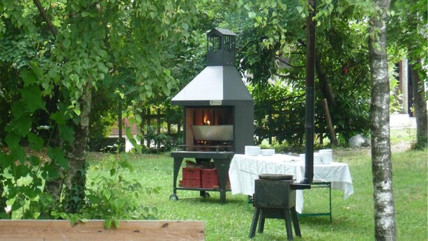 Een buiteneetgedeelte met een barbecue, een tafel met witte tafelkleed en een houten bank.