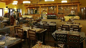 Een restaurant met meerdere eettafels, houten balken in het plafond en een bar met flessen op de planken.