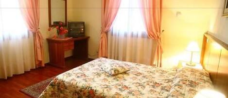 Une chambre à coucher avec un lit, un bureau, une lampe et des rideaux.