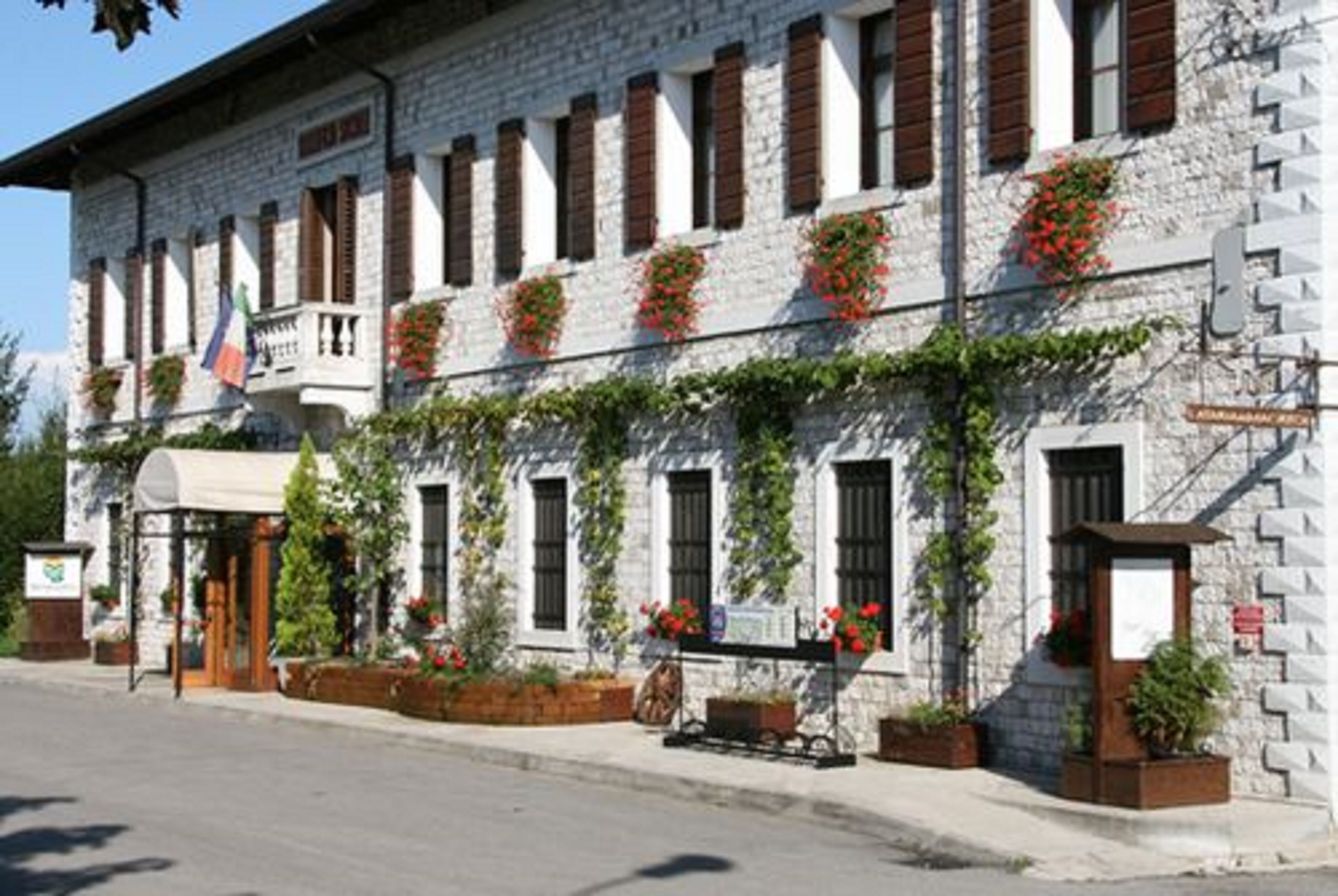 Il s’agit d’un bâtiment en pierre doté de nombreuses fenêtres, dont certaines sont pourvues de volets, et d’un balcon. Des jardinières remplies de fleurs rouges ornent les rebords des fenêtres.