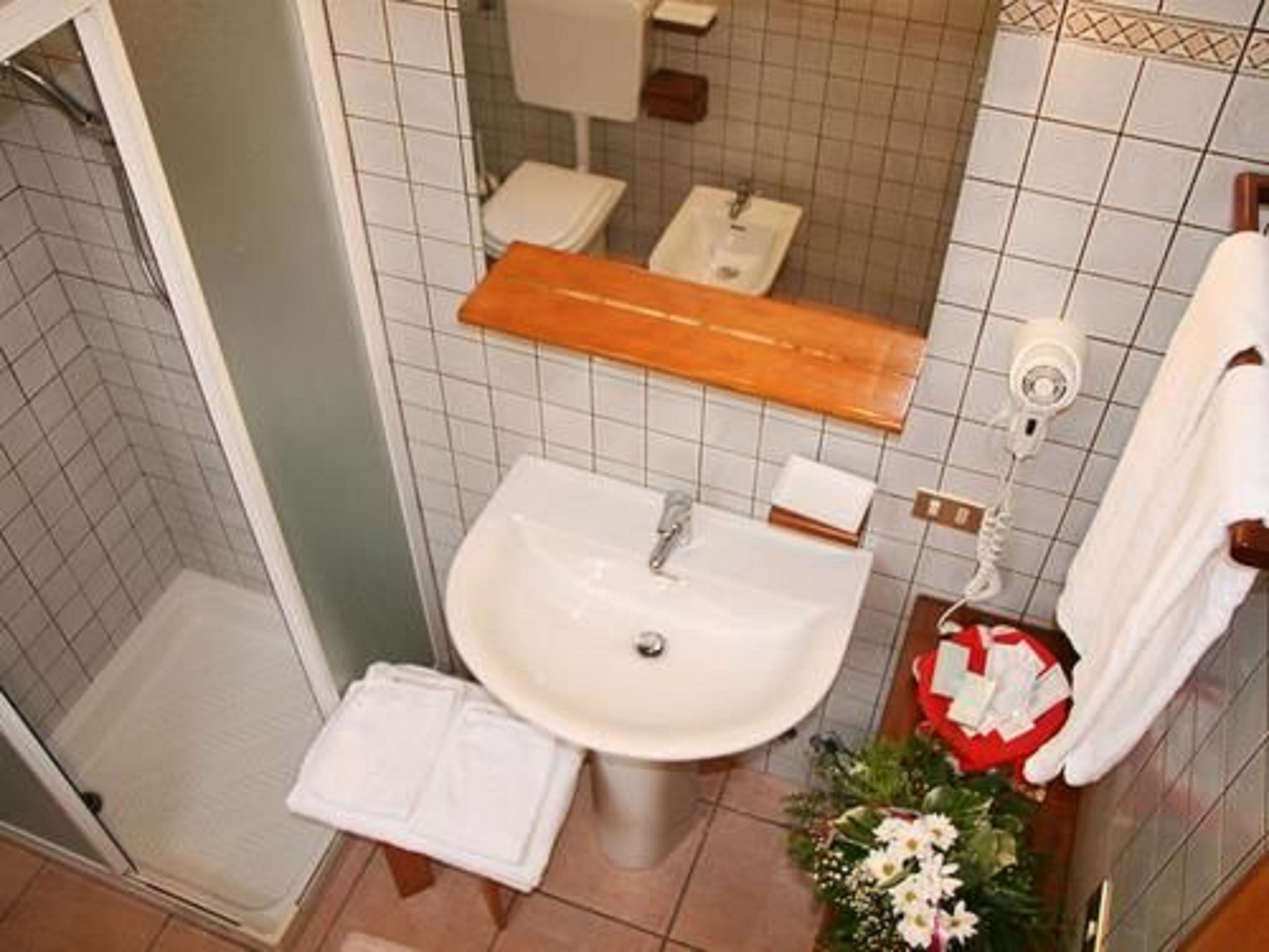 A bathroom with a sink, toilet, and shower. There is a towel rack with a white towel and a red and white decoration.