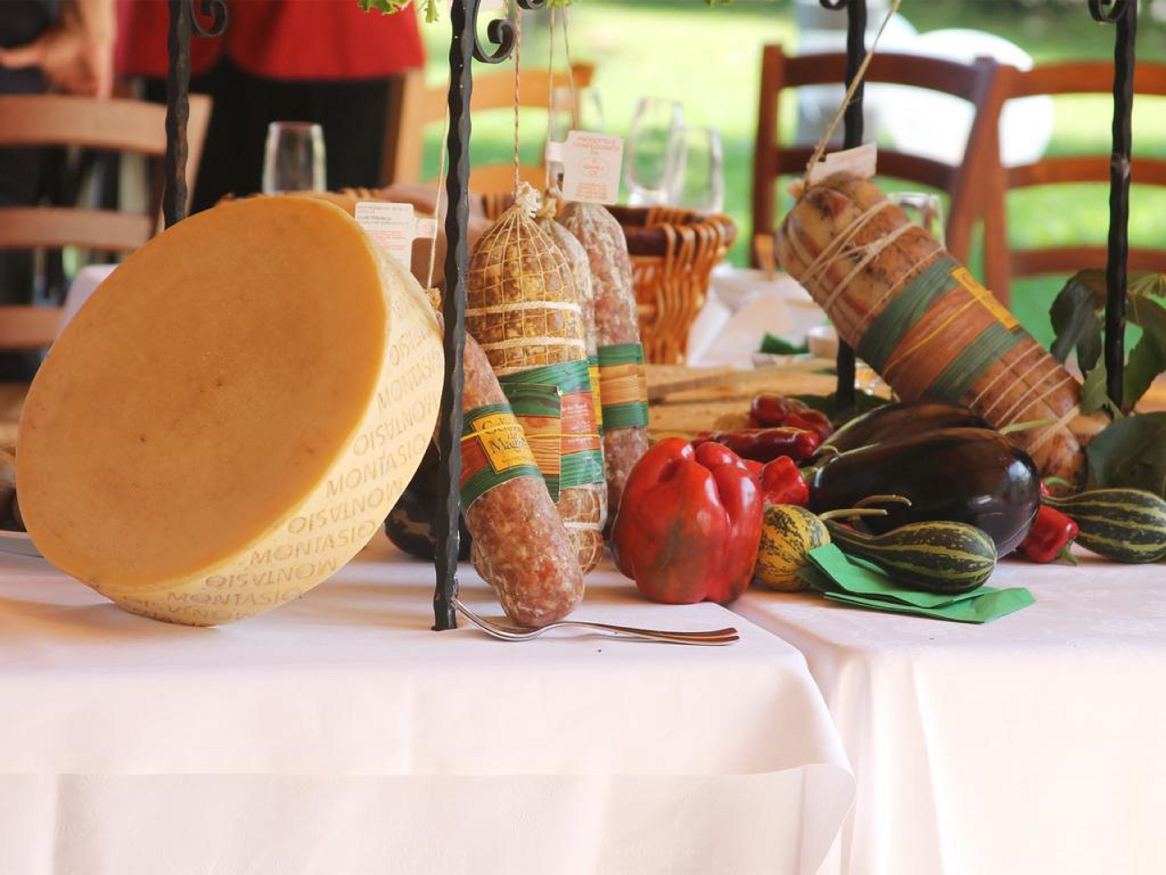 A table with a large wheel of cheese, several types of cured meats, and fresh vegetables.