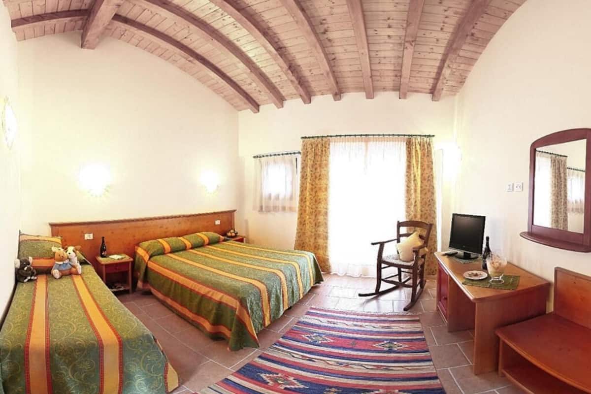 Un dormitorio con dos camas, techo de madera, televisor, mecedora y escritorio con silla.