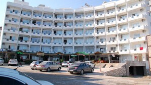 A multi-story hotel with balconies, a parking lot, and several storefronts. - Hakan Apart Hotel (Erdemli)